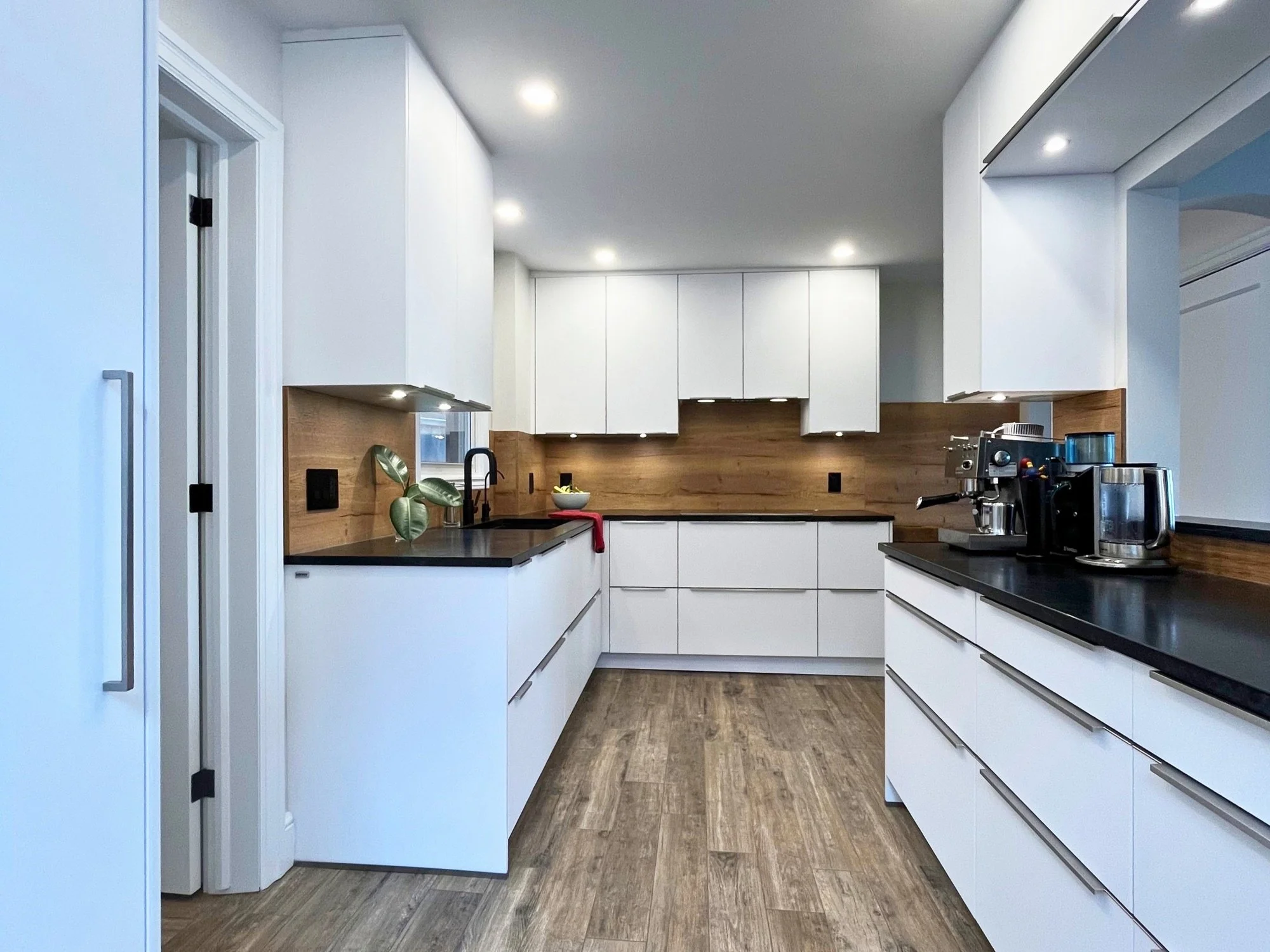 Modern European kitchen featuring white handleless cabinetry, wood accents, and a sleek black countertop.