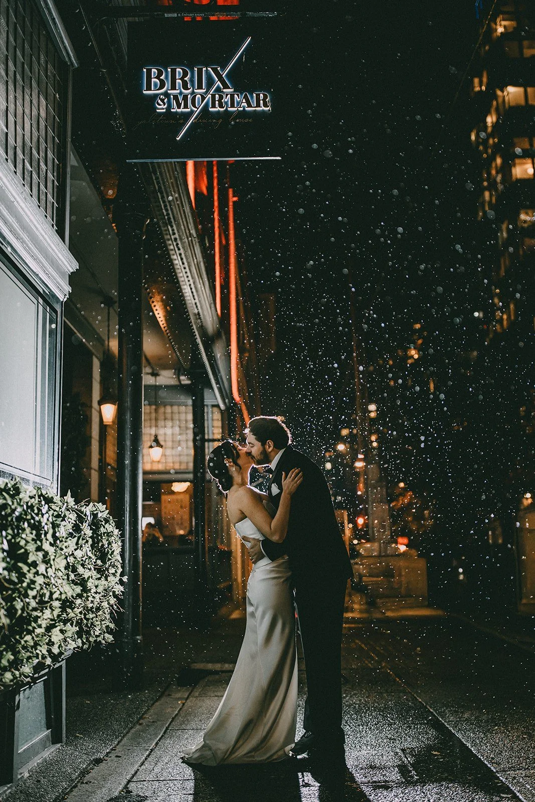 Bride and groom kiss in the rain outside Brix & Mortar in downtown Vancouver at night