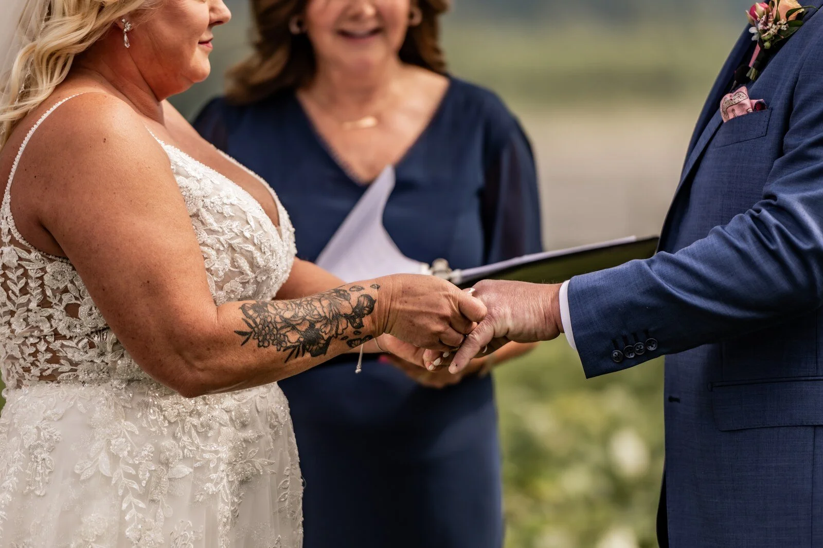 A wedding officiant reads from her ceremony book while a couple hold hands during their outdoor BC wedding ceremony
