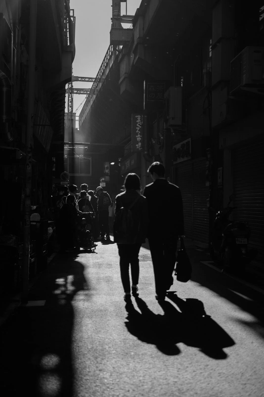 Early light in the gap between the Ueno train tracks and the market with commuters and market-goers, shot on a vintage 50mm.
