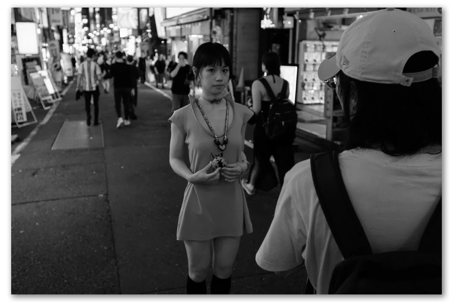 Street photograph made in Shinjuku, Tokyo — a young women posing for her boyfriend, evening light