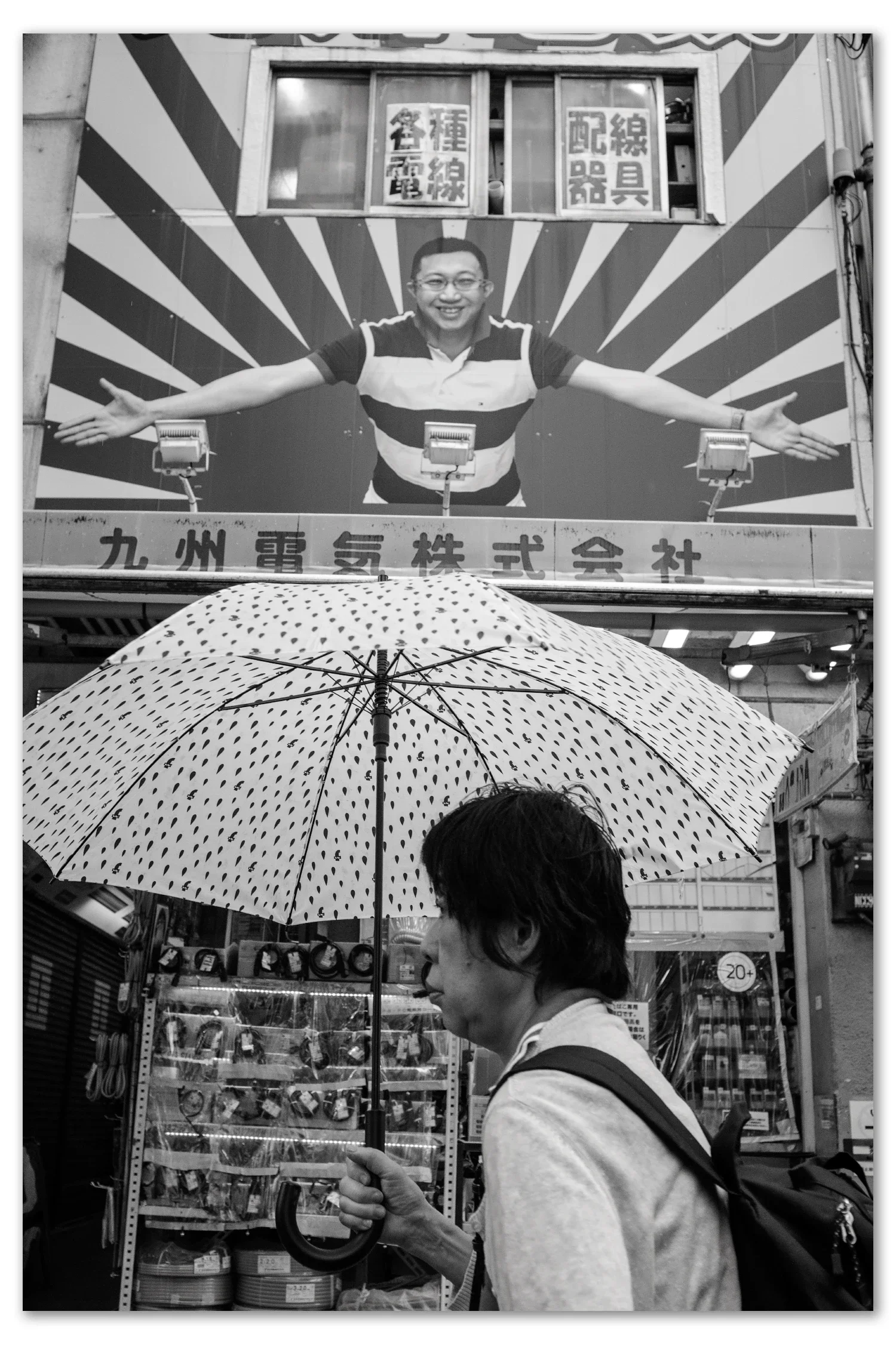 A woman passes by a famous Akihabara sign on a rainy day, carrying an umbrella shot with a vintage 35mm Nikkor lens.
