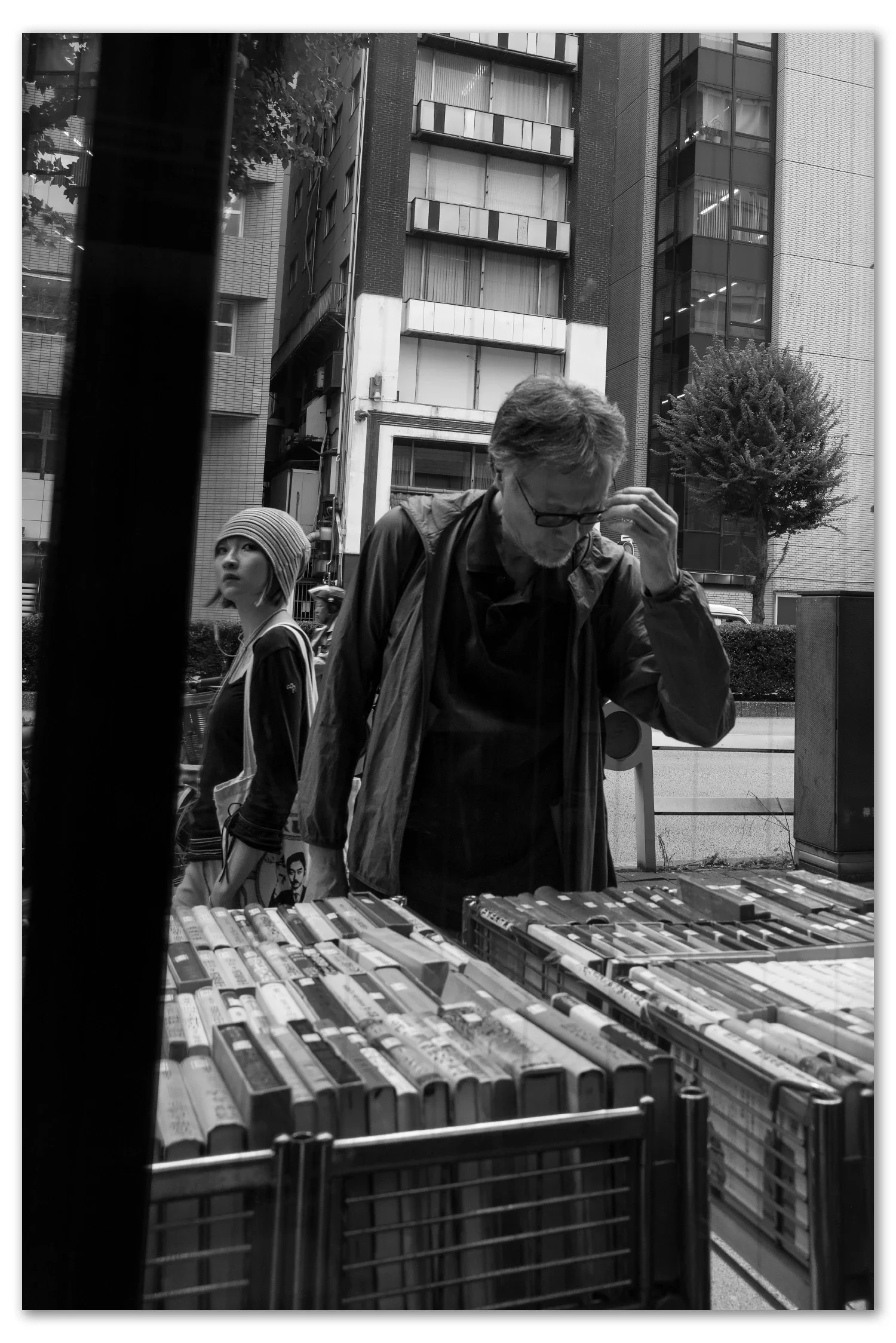 An older man in a vest leafing through a book at an outdoor bargain cart in Jimbocho book town