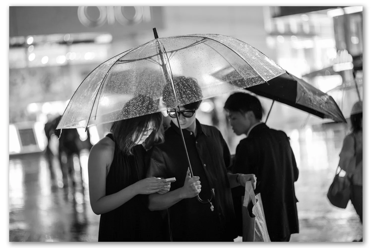Three people huddled under clear umbrellas outside Yurakucho Station in heavy rain