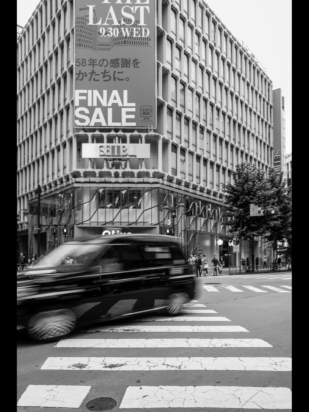 A black taxi blurs across a zebra crossing in front of Seibu Shibuya on its final day, a banner reading THE LAST 9.30 WED and FINAL SALE above the entrance, forged at 28mm