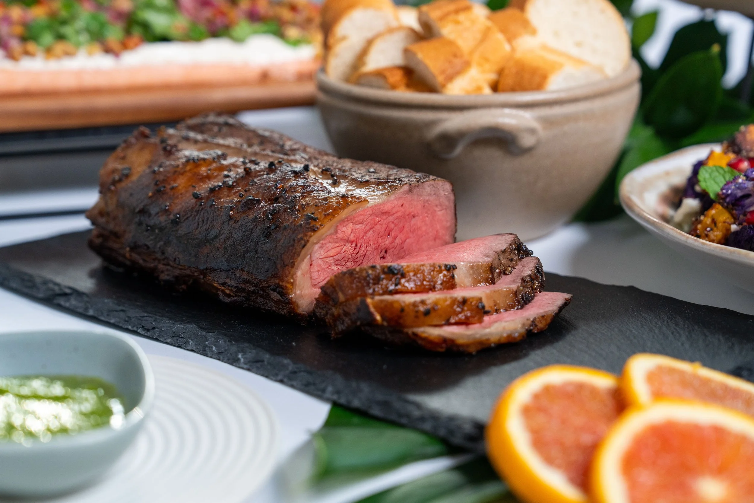 A buffet of grilled meats, vegetables, salads, and desserts displayed on a white and black stand outdoors with a blurred autumn background.