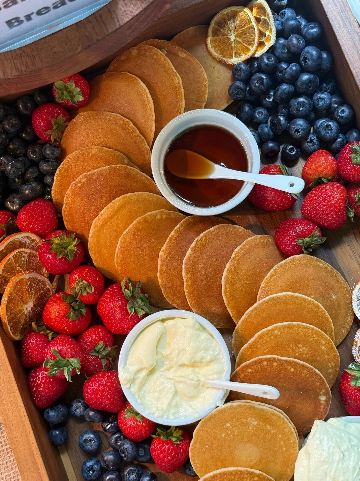 A breakfast tray with fried dough, fresh strawberries and blueberries, dried orange slices, syrup, and cream.