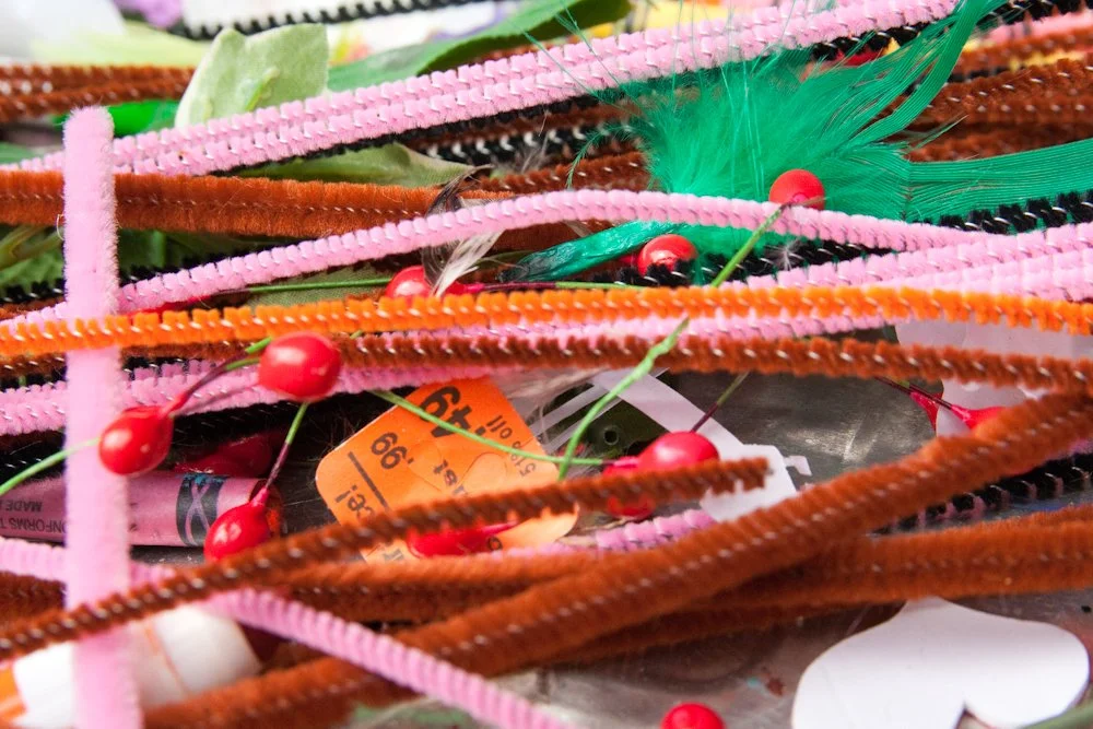 A close-up of colourful craft supplies, including pipe cleaners, beads and feathers.