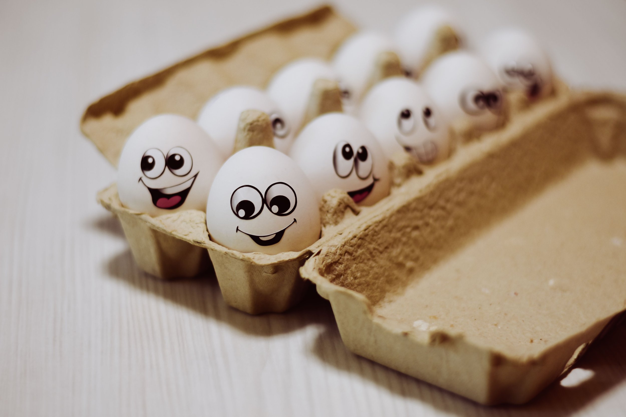 A carton of eggs with various facial expressions drawn on them.
