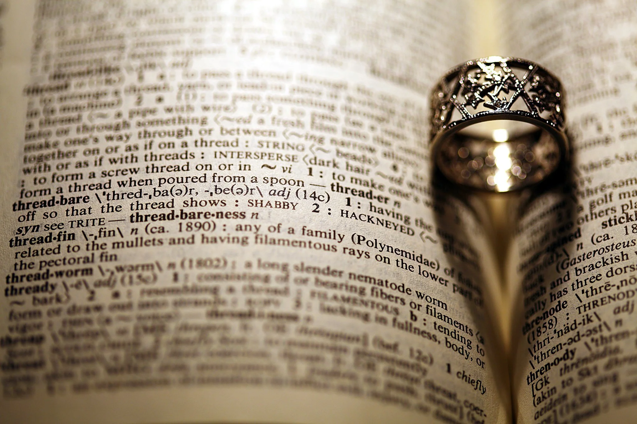 A ring rests on the page of a dictionary, open to the definition of the word, threadbare.
