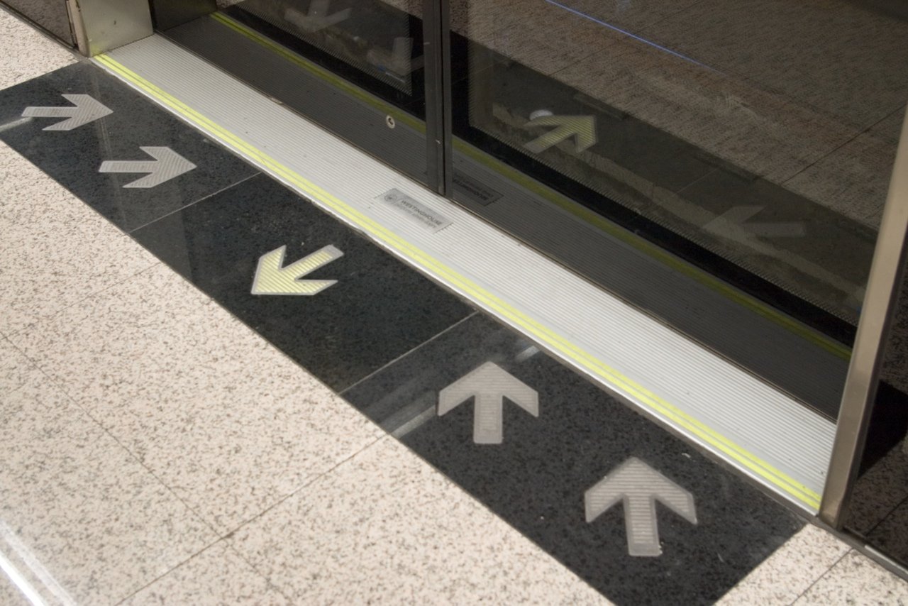 Five arrows point in different directions in front of an automated glass door to the Beijing Metro.