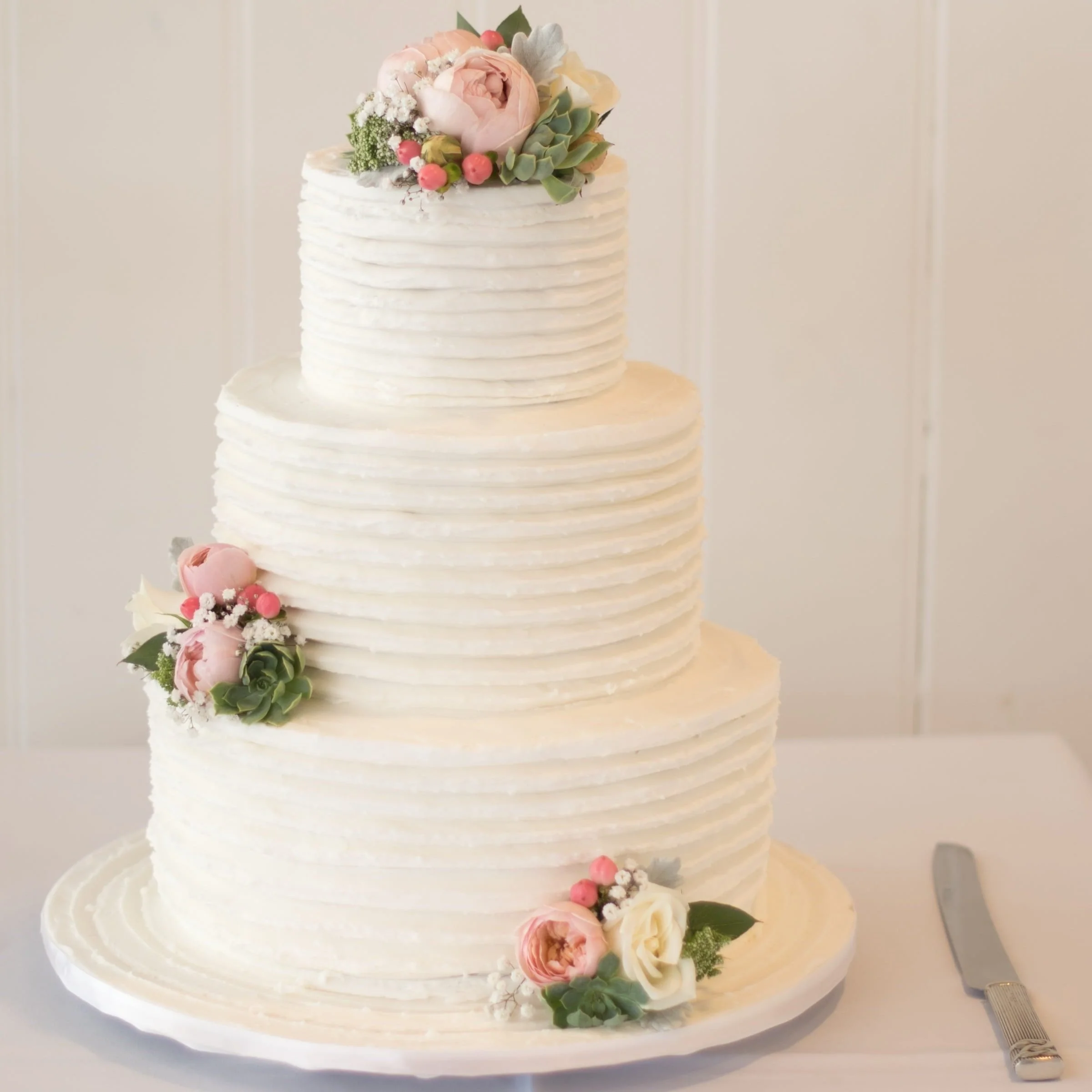 A white iced three-tiered wedding cake decorated with floral arrangements.
