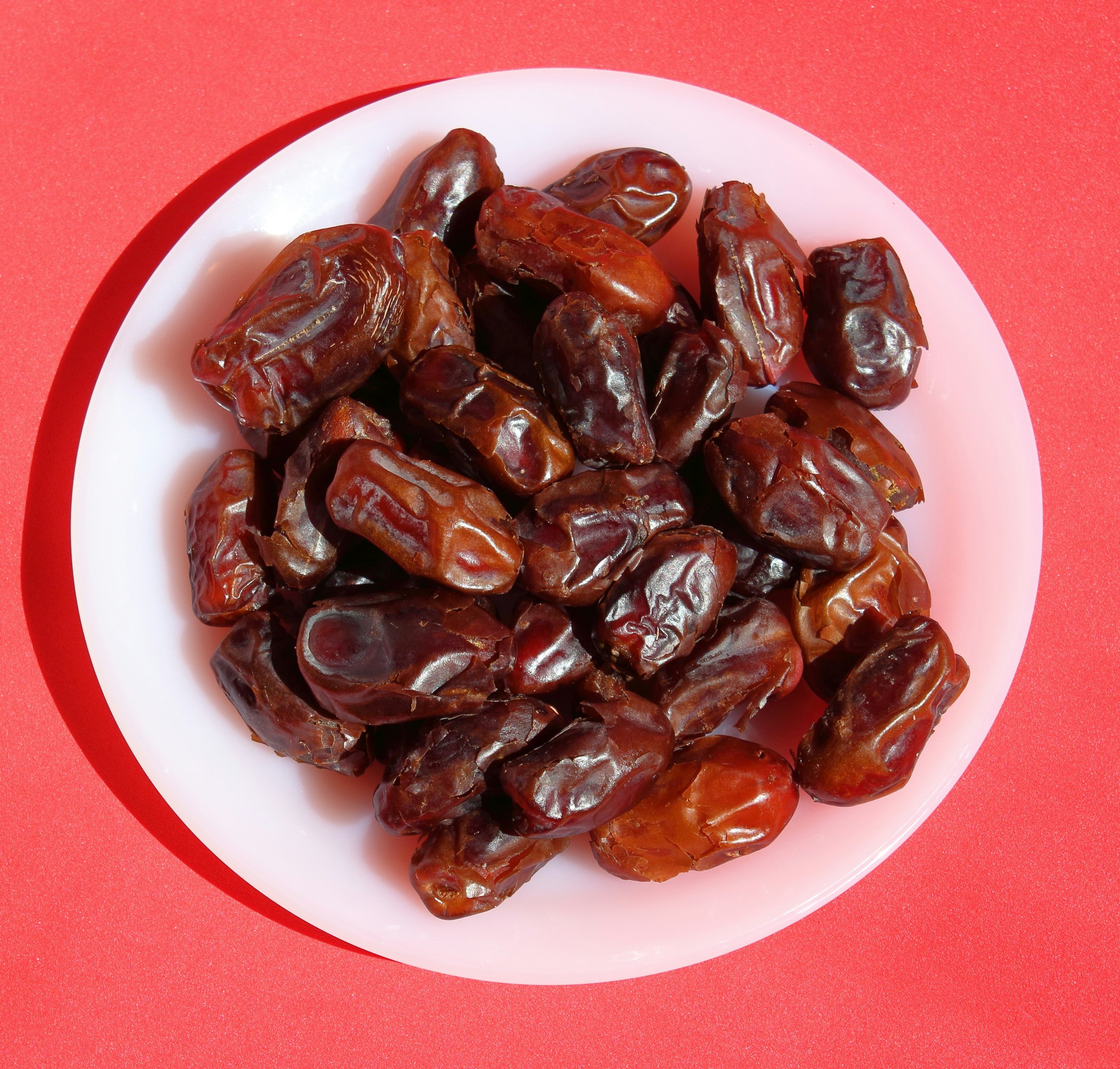 A white plate is topped with fresh dates. The plate sits on a peach-coloured benchtop.