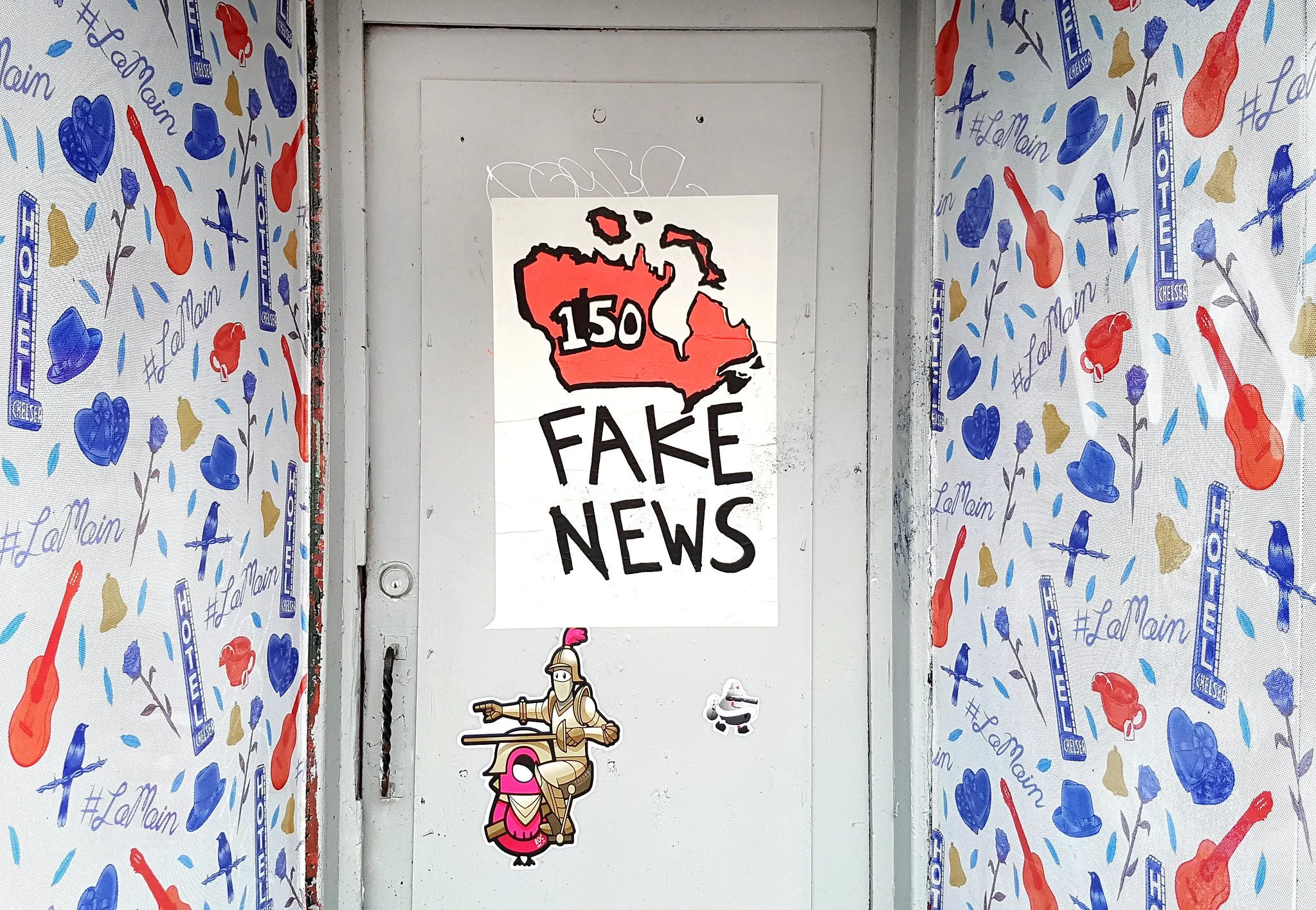 A white door has a poster on it that says Fake News. The walls on either side of the door advertise Hotel Chelsea and include images of blue hats, red guitars and gold bells.