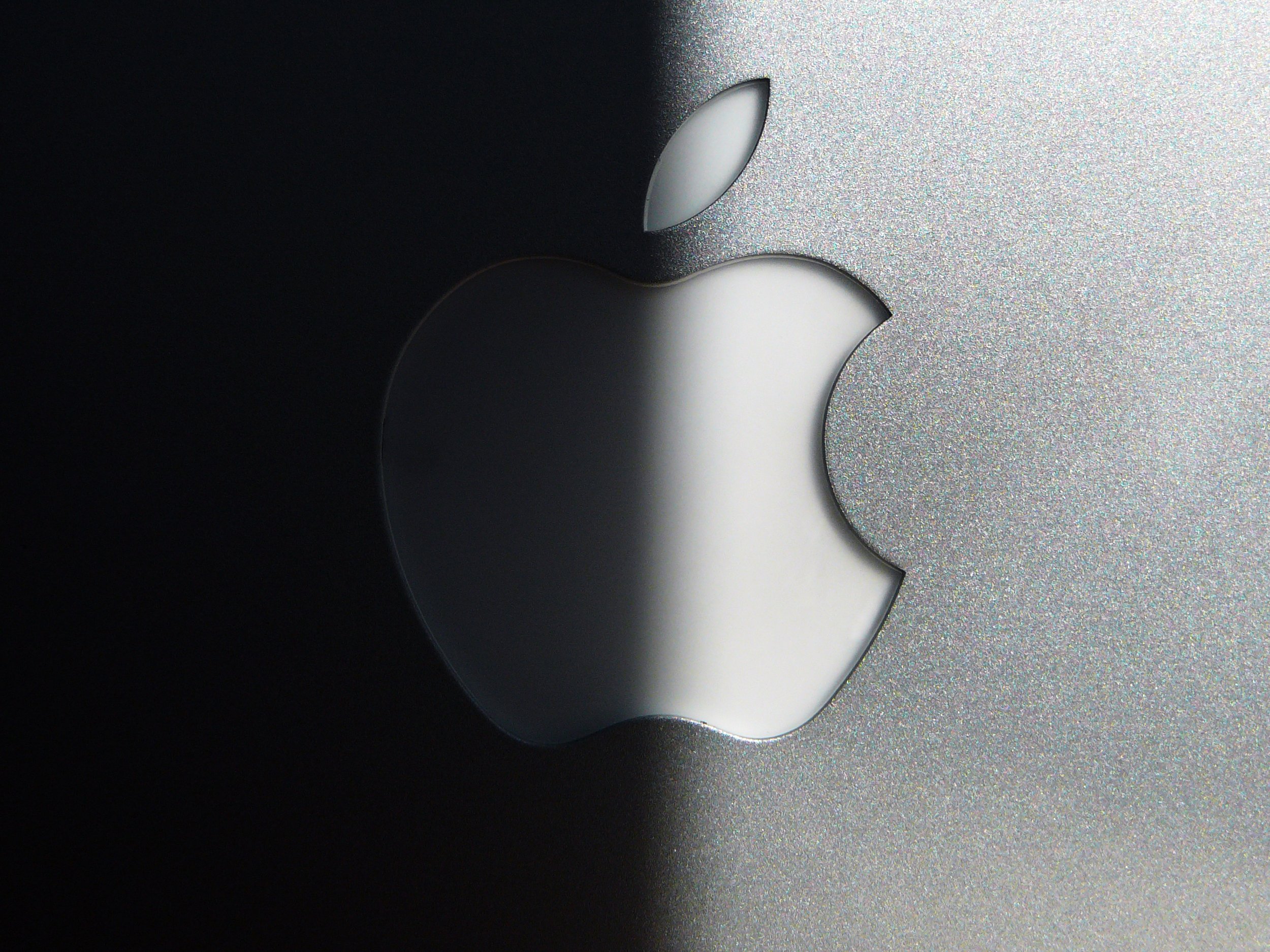 The lid of an open Mac laptop shows the Apple logo close up. Half of it is in shadow.