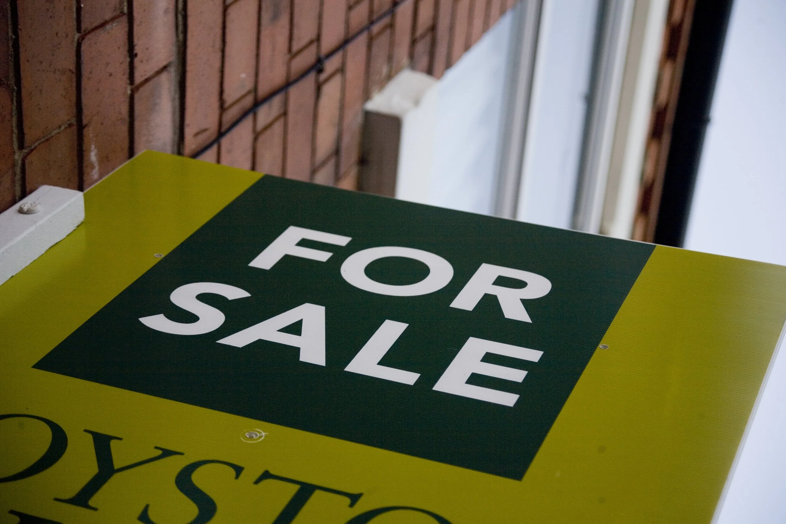 A for sale sign outside a red-brick house.