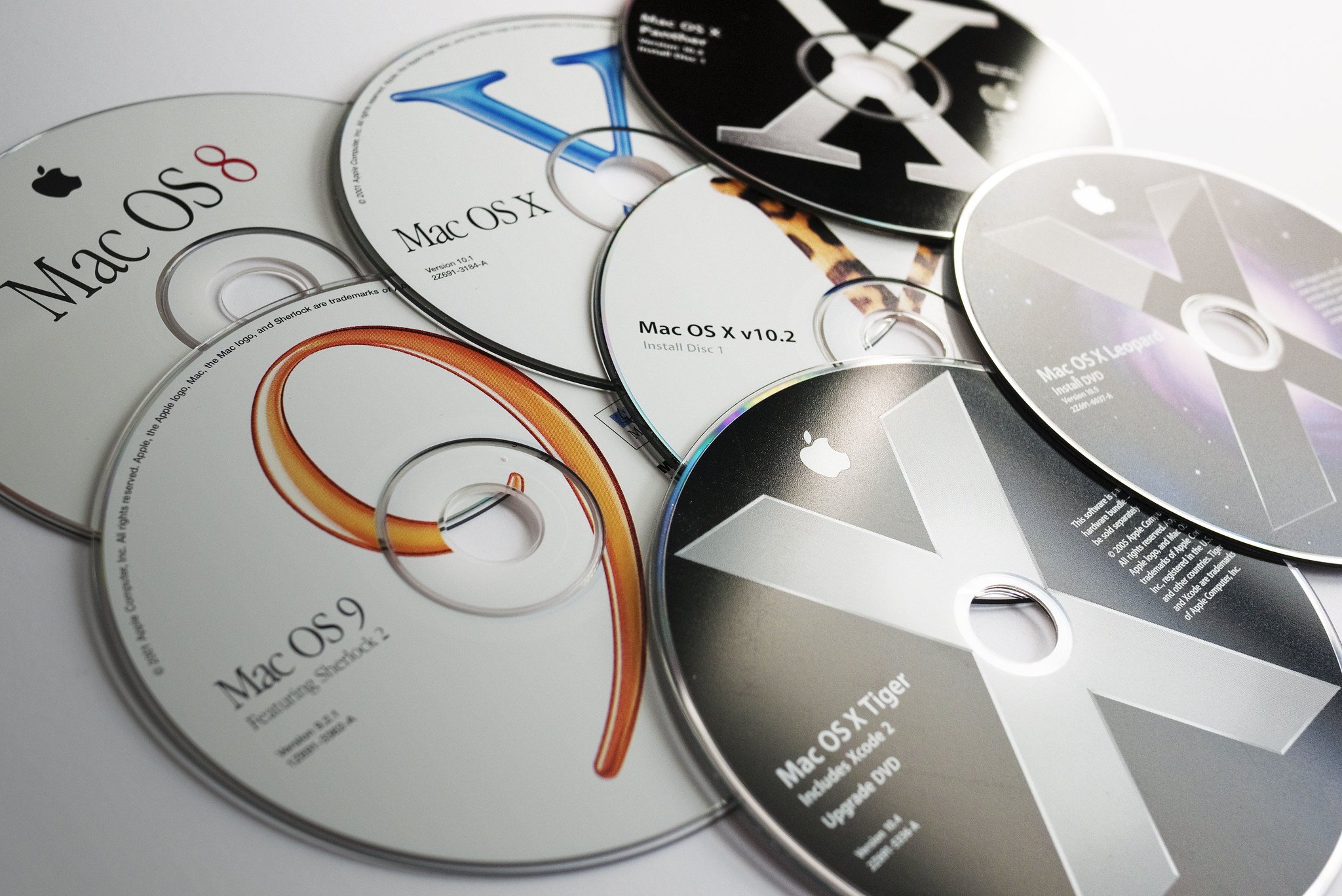 A selection of software discs for Mac lie strewn on a white desk.