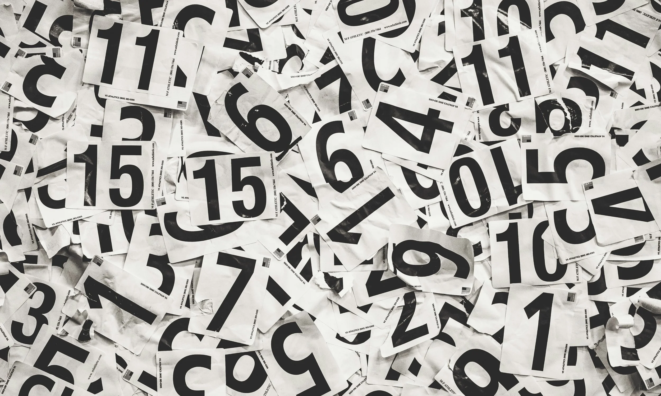 Different numbers are written in black text on white paper. They sit piled and jumbled up.