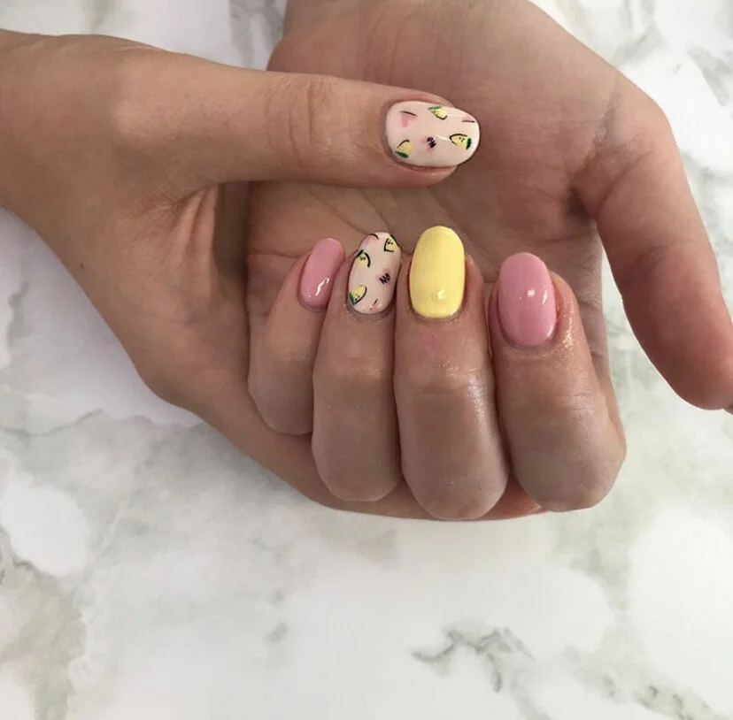Close-up of a hand with decorated nails, featuring floral and abstract patterns, one solid yellow nail, and pink polish.