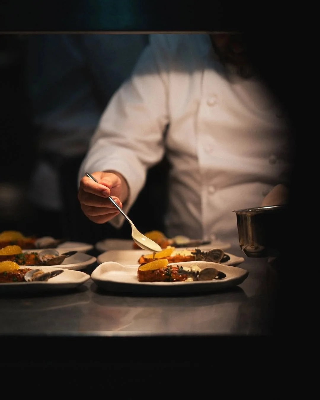 Chef plating dishes in a professional kitchen, focusing on carefully placing garnishes on plates.