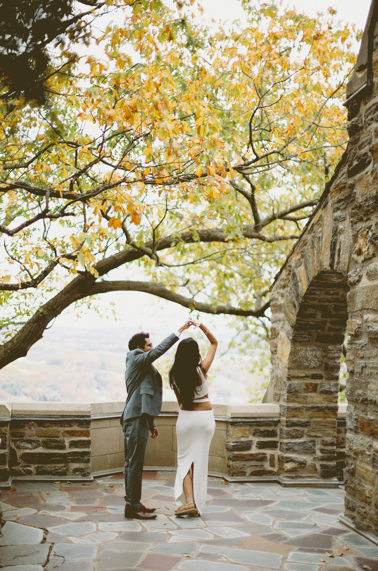The future groom spins his bride in circles with the rolling hills and fall trees surrounding them.