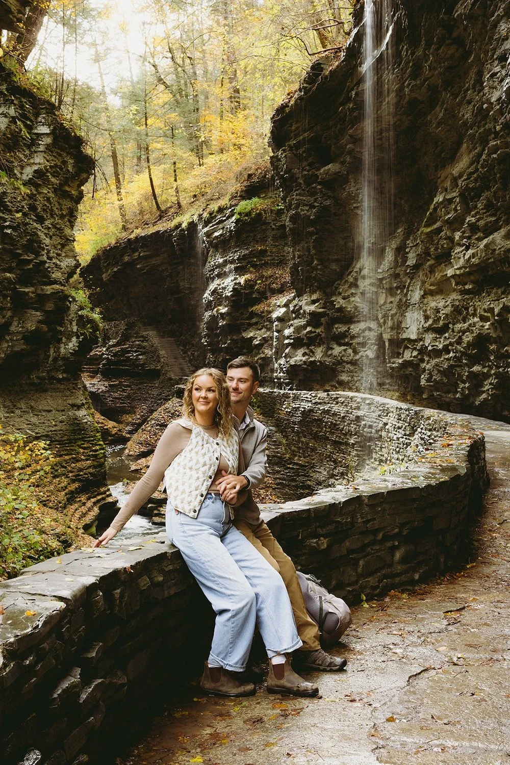 The couple sit on the ledge of the gorge admiring the scenery with the falls just behind them.