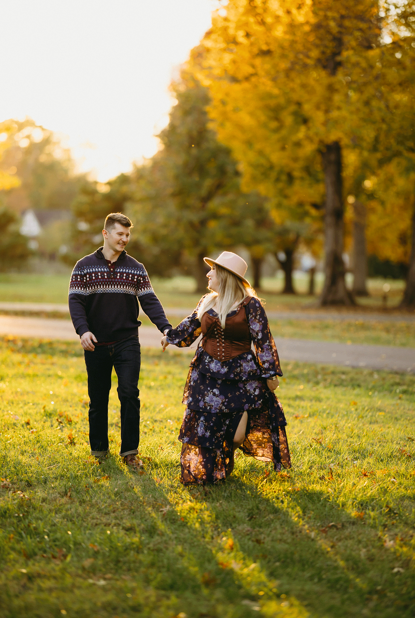 The couple run hand in hand together through the park.