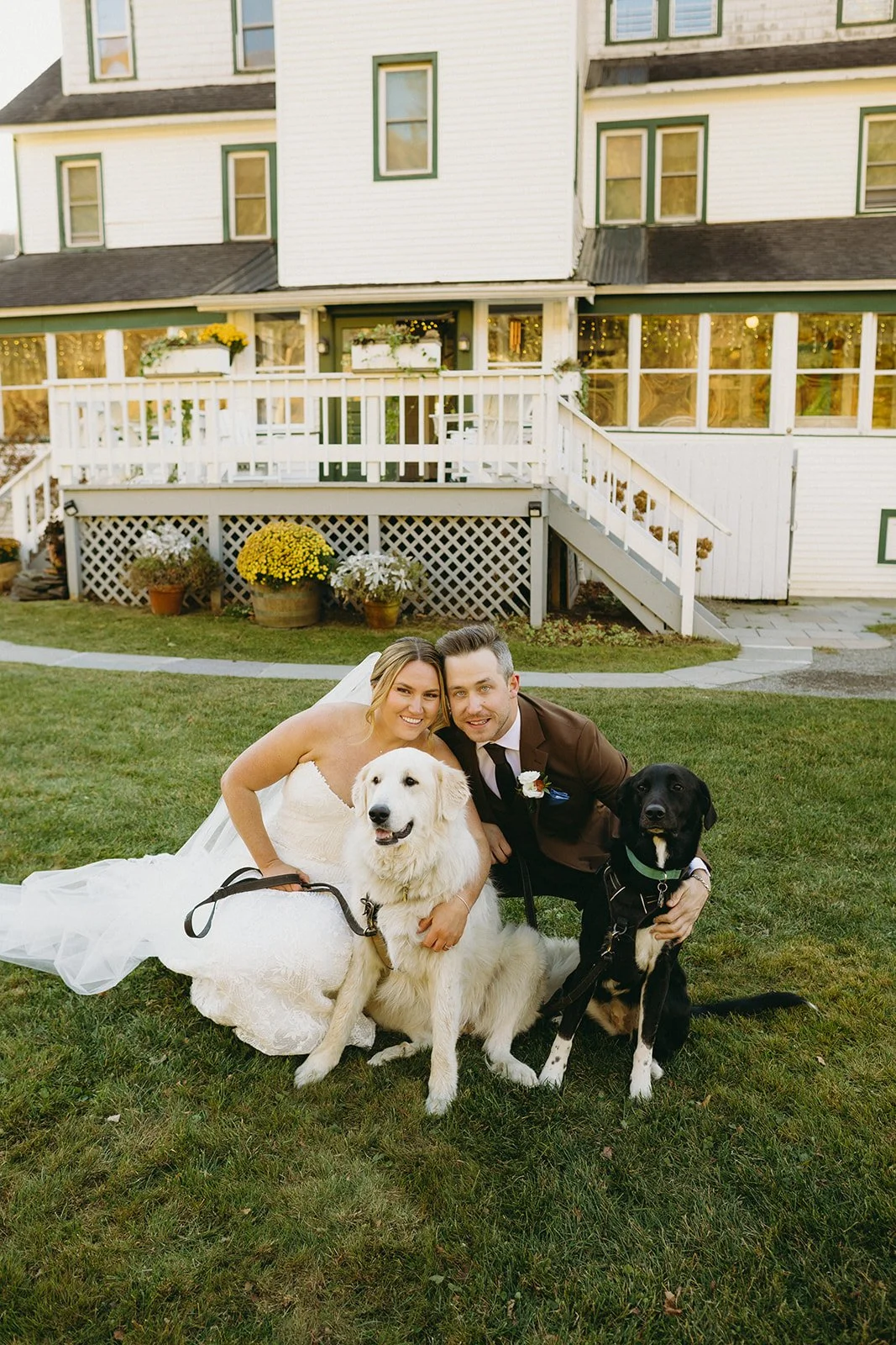 The bride and groom pose with their pups in front of the wedding venue