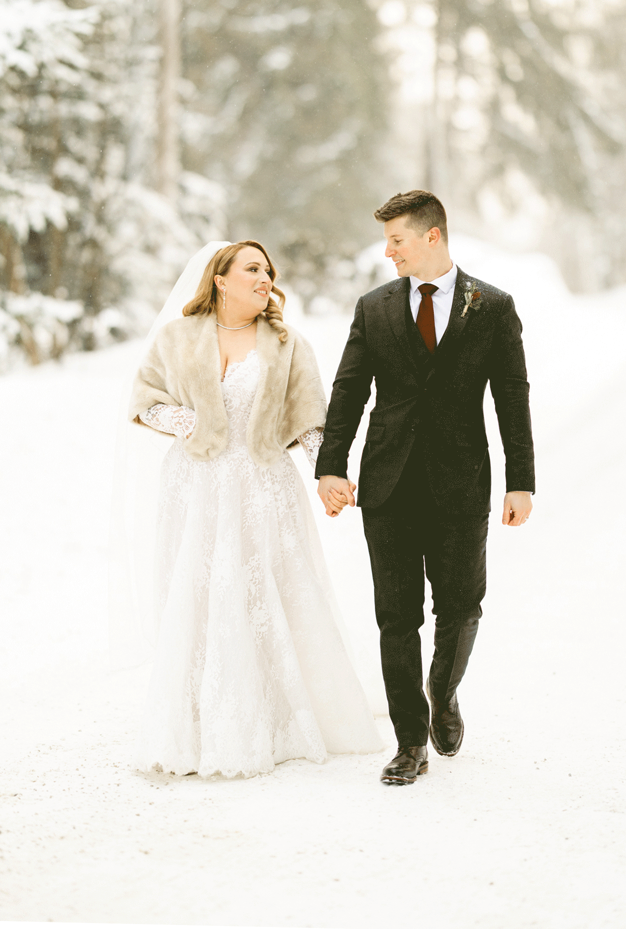 The bride and groom walking the snowy trail as the groom hip bumps his bride.