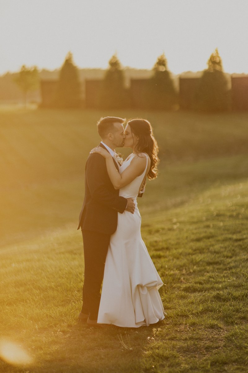 Bride and groom kissing during the golden hour in the winery field.