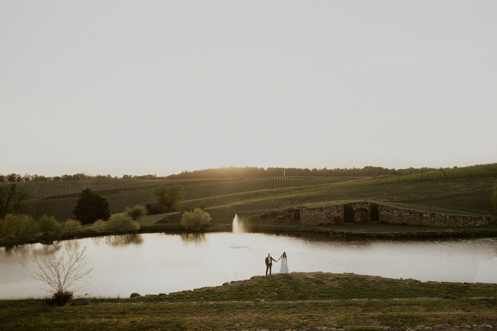 Couple standing infront of pond while the sun sets.