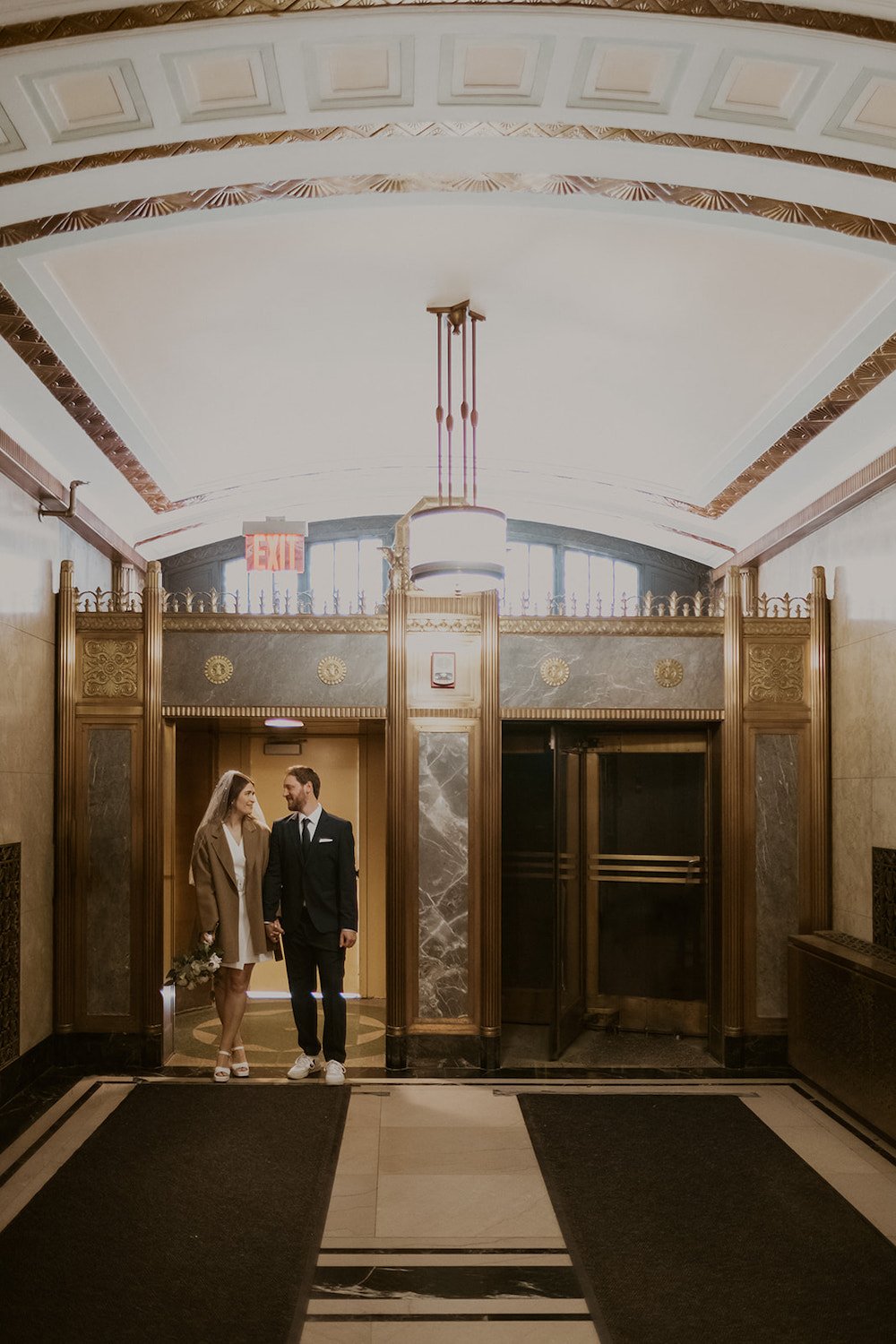 Bride and Groom standing in the door way of the courthouse. Surrounding with hints of gold framing and turn-style doors. 