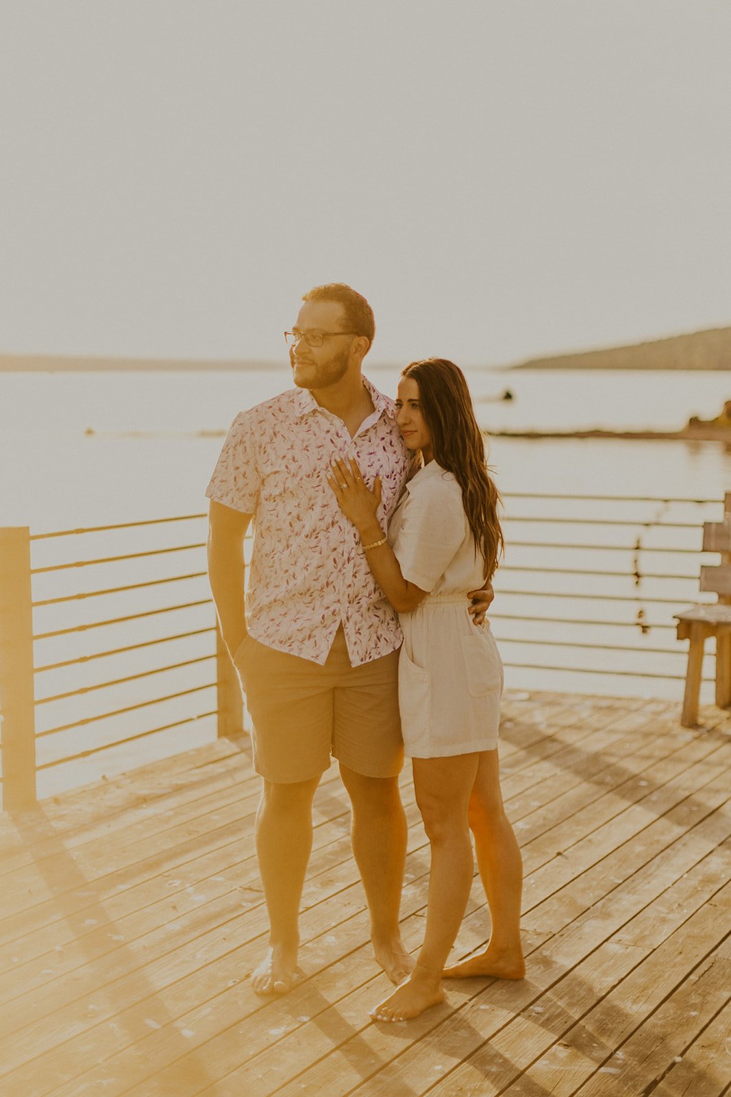 Couple standing on pier overlooking the lake together.
