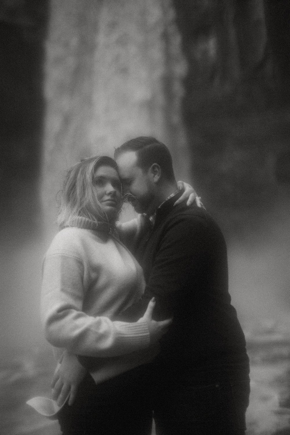 Black and white photo of couple standing infront of waterfall.