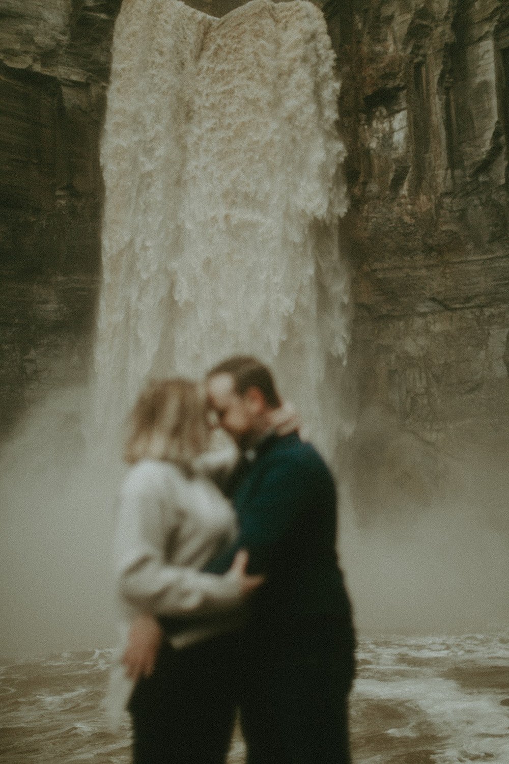 Couple holding one another infront of a boisterous waterfall.