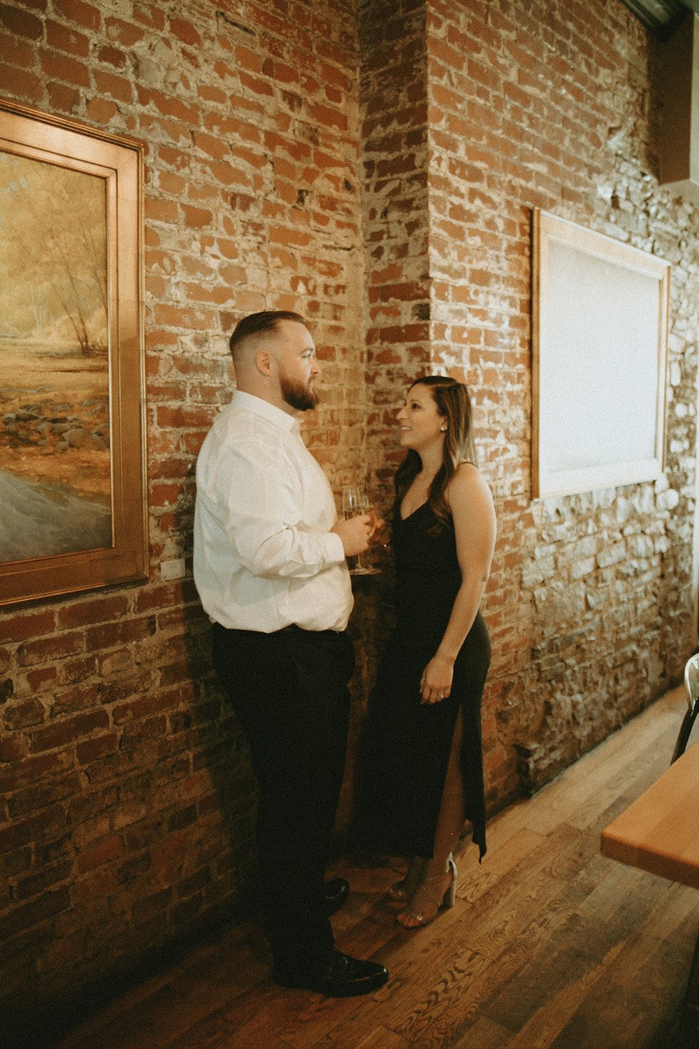 Couple standing in Hand in Foot leaning against the brick wall enjoying a cocktail.
