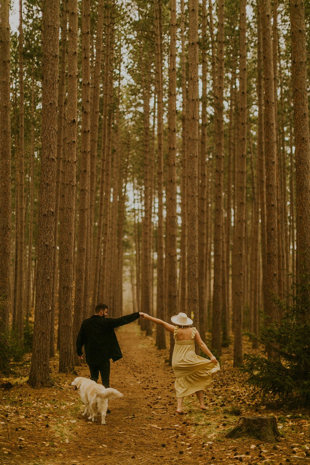 Couple walking through the trees with their dog following behind.