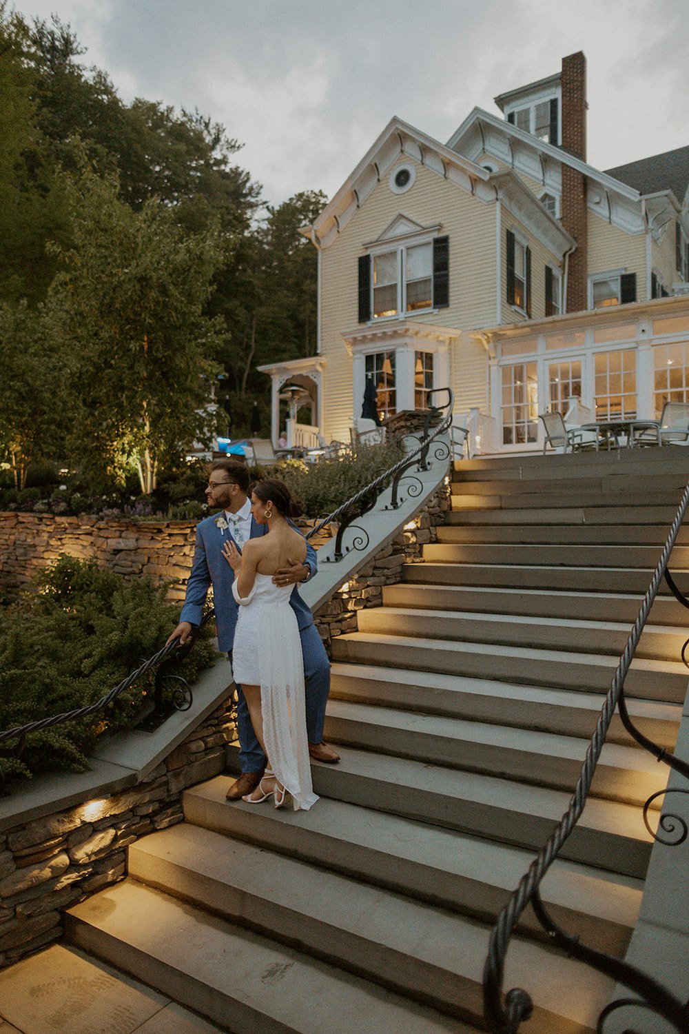 Bride and groom stand together on stairs looking out at the lakeside view during blue hour.