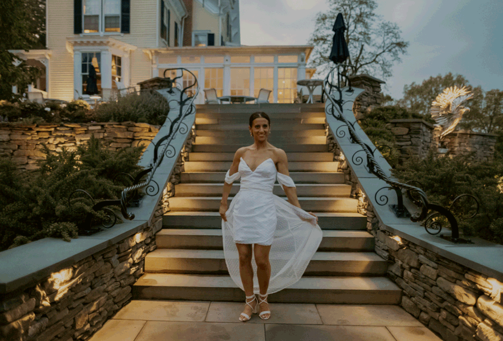 Bride twirls in her after-wedding party dress infront of the stairs at the Inn at Taughannock.