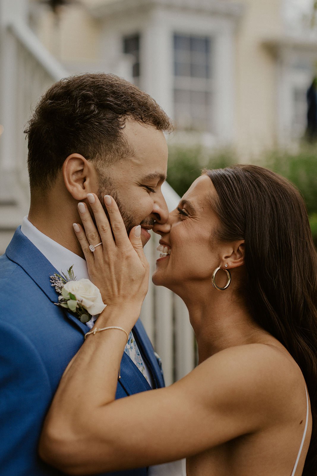 Bride holds her grooms face while smiling to sneak a kiss. 