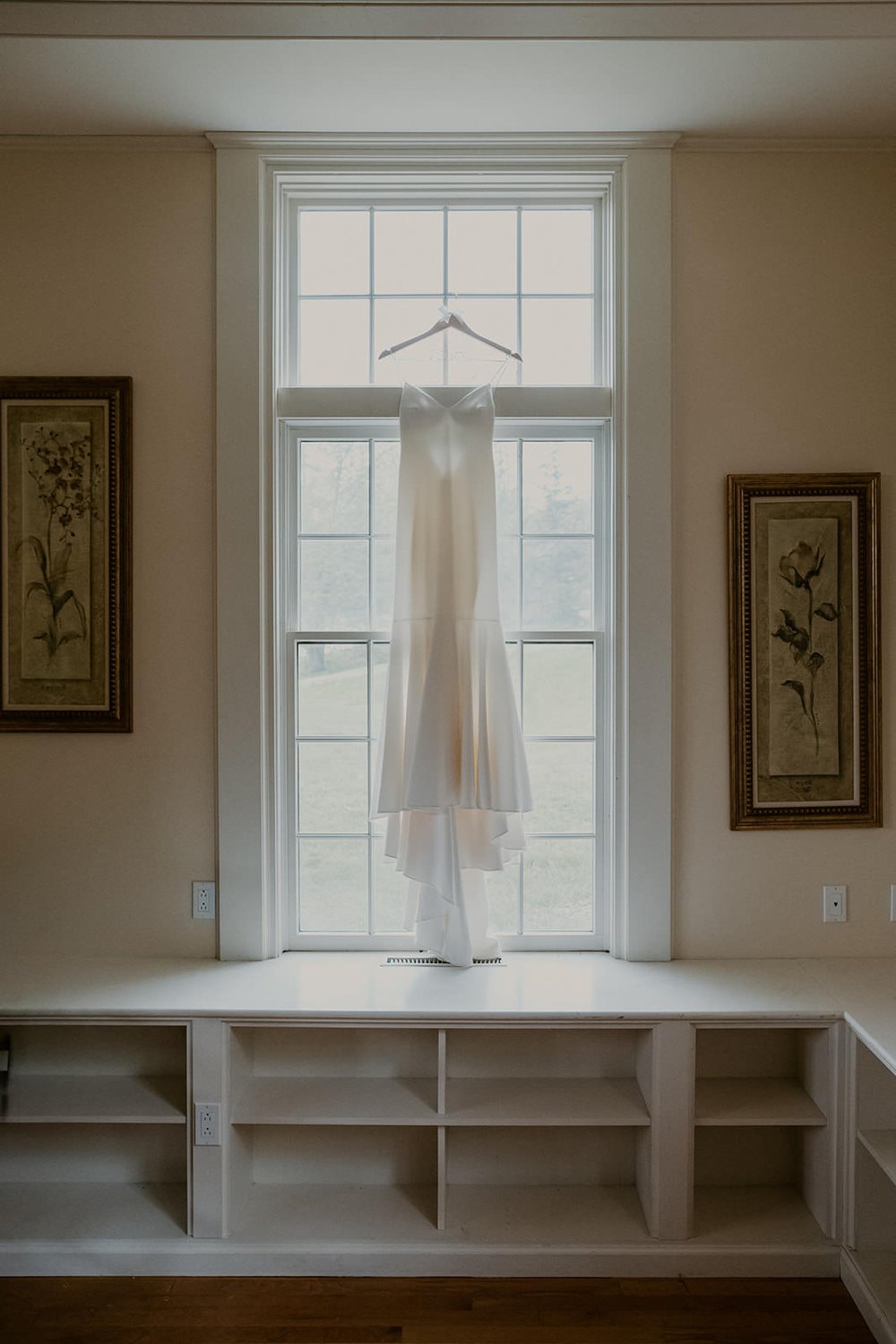 Bridal gown hanging infront of window as it gleams with beauty.