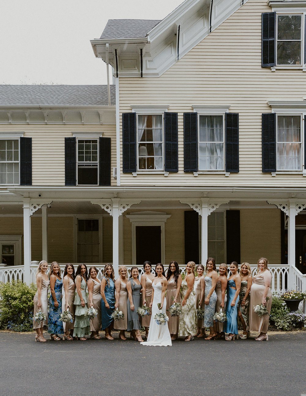 The bridesmaids &amp; bride stand infront of the Inn at Taughannock venue for a full party portrait.