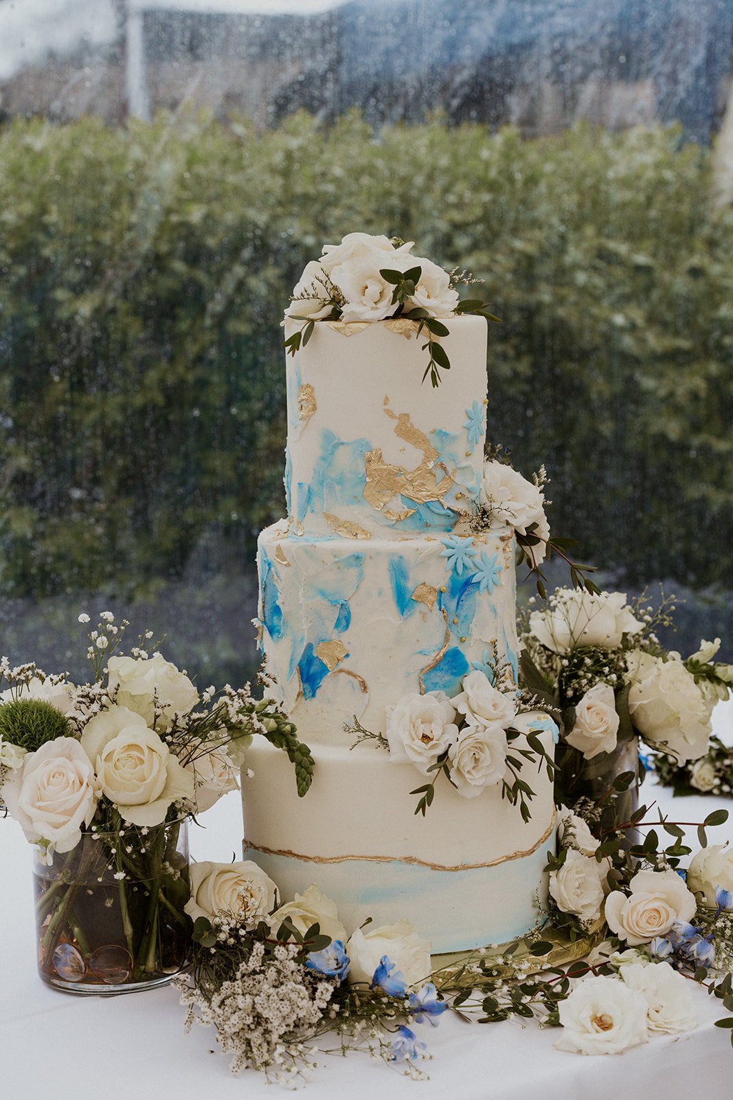 Bride and Grooms wedding cake dressed with florals, touches of blue and gold throughout the three tier cake.