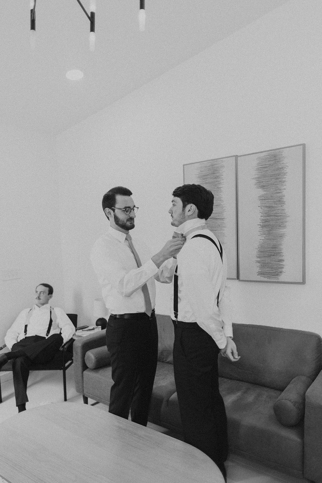 The groom assisting one of his groomsmen's with tying his bow-tie.