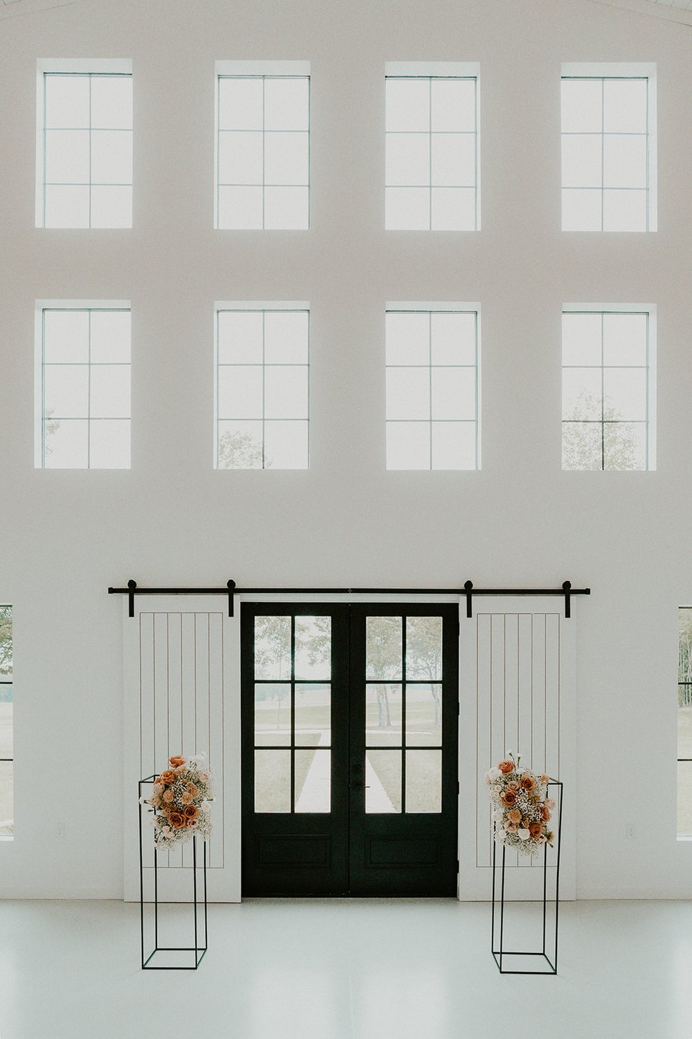 Ceremony aisle with hanging arrangements and black double doors. 