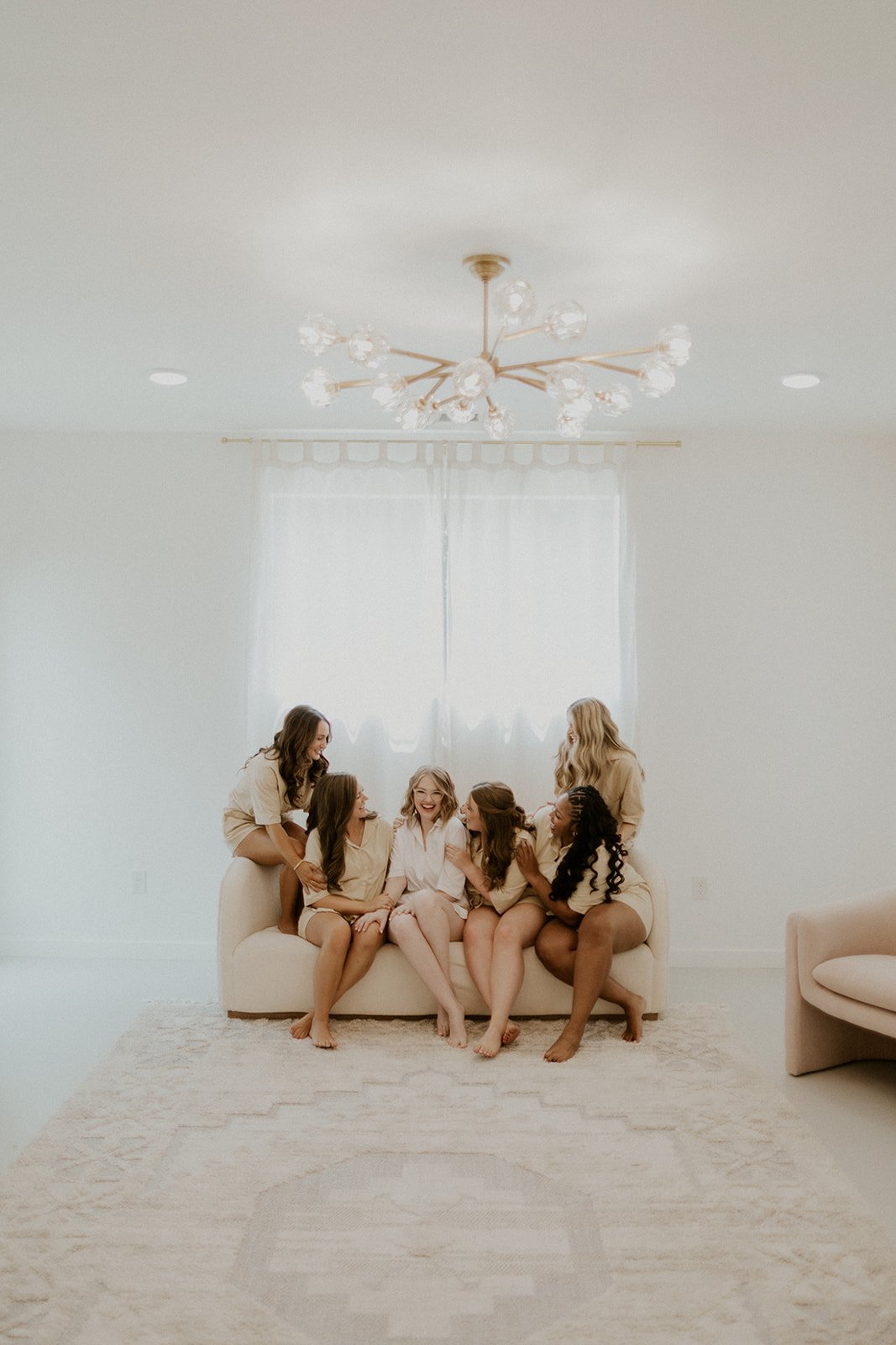 Bridesmaids posing together in the bridal suite. Sitting on the couch together laughing.