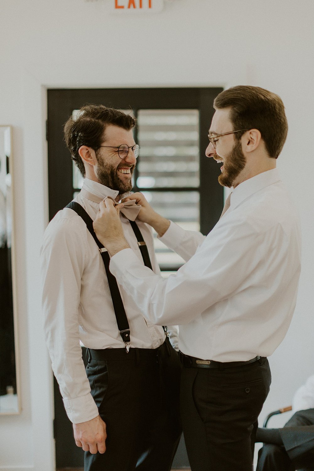 Groom assisting one of his groomsmen with tying his bow-tie.