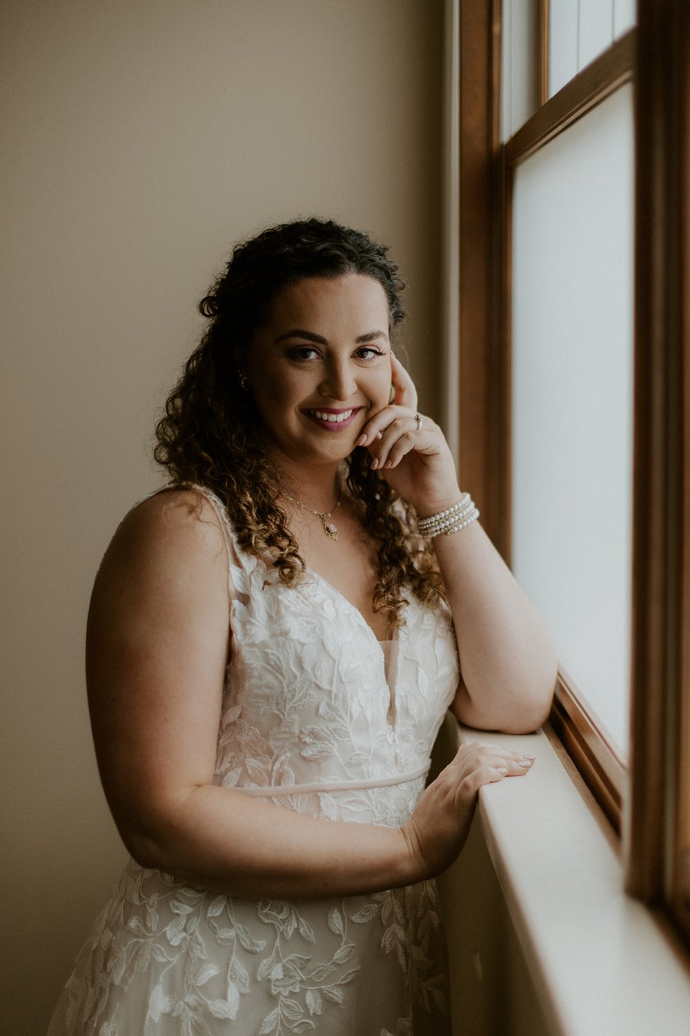 Bride stands at windowsill with a enchanting smile.  