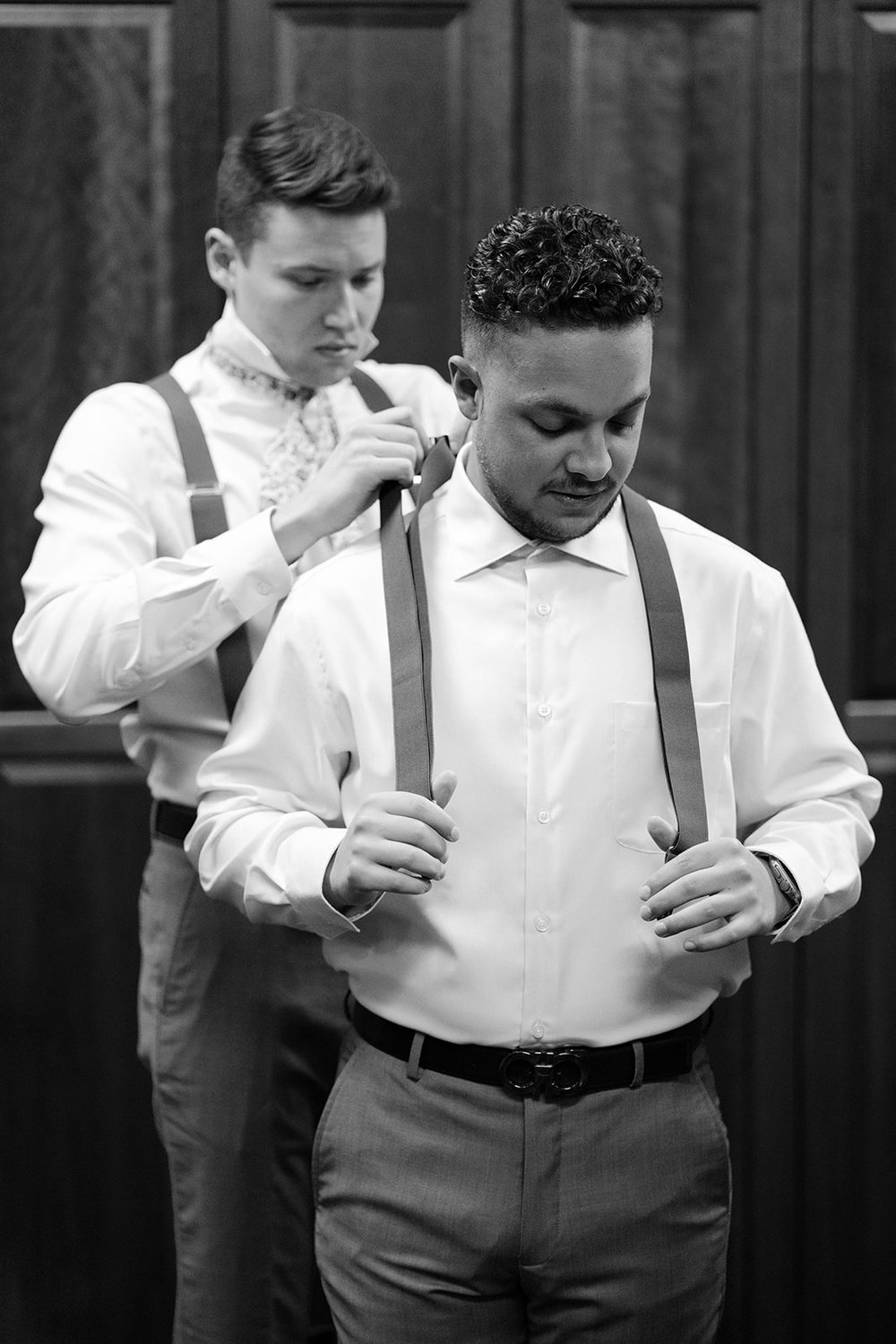 Groomsmen assist one another in adjusting their suspenders. 