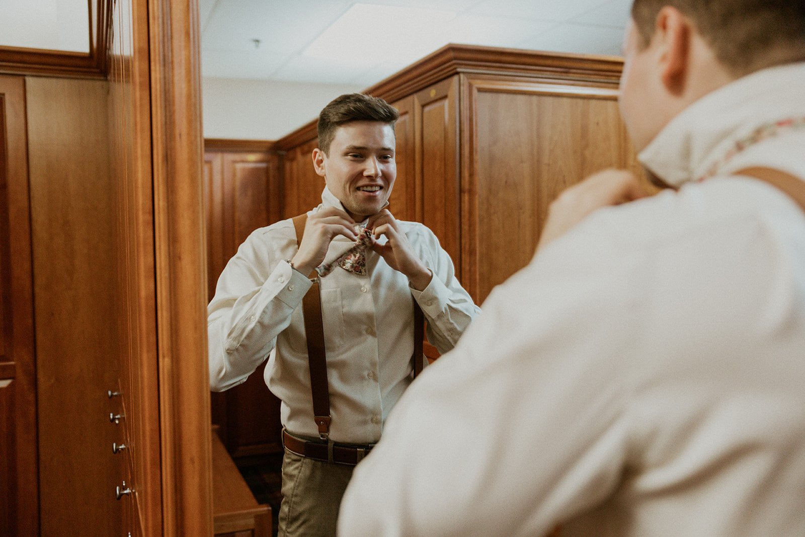 Groomsmen looks at himself in the mirror while tying his bow tie.